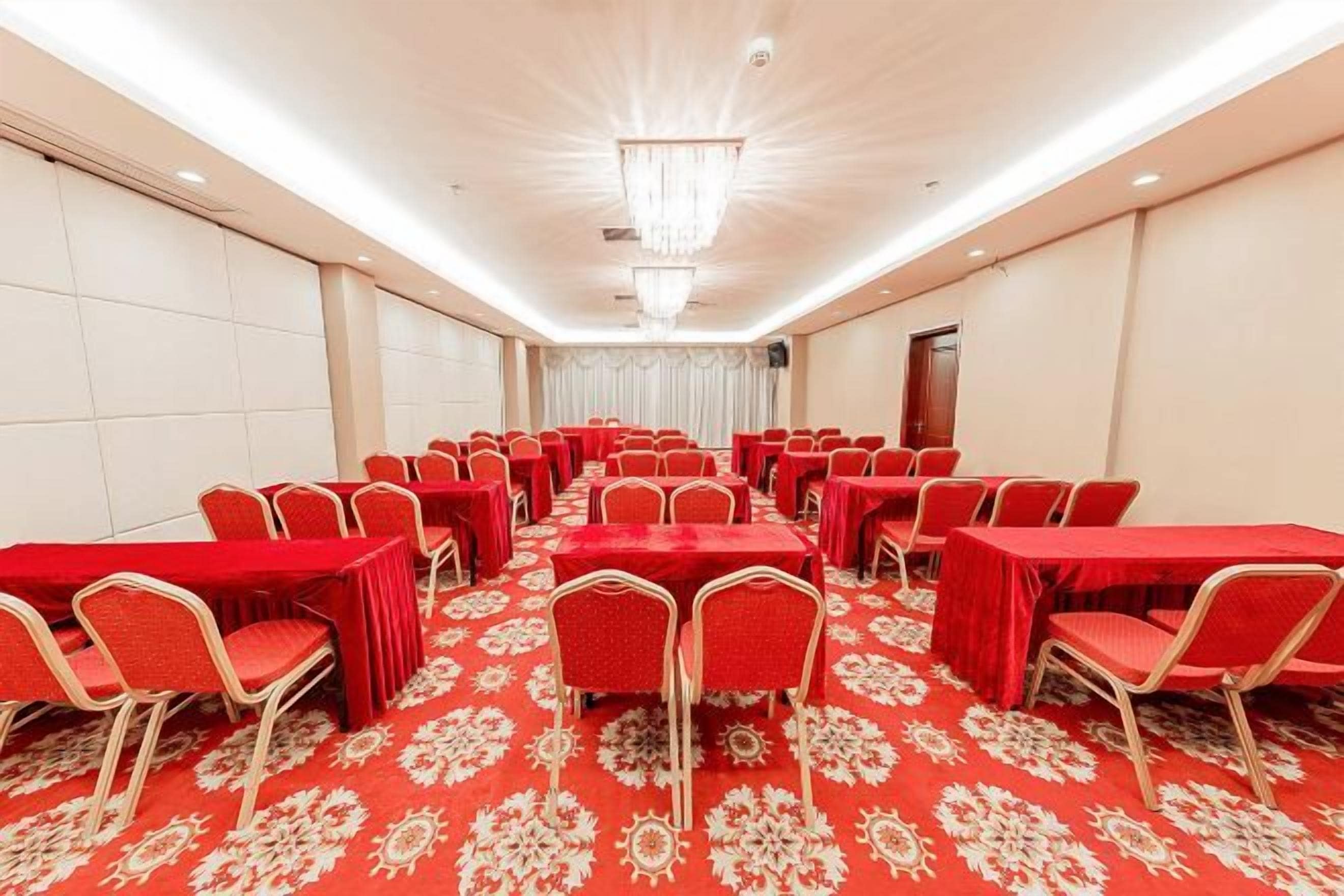 Une salle de conférence avec des rangées de tables et de chaises, un sol recouvert de moquette et un lustre.