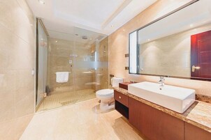 Un baño moderno con ducha de vidrio, un lavamanos blanco y un espejo grande.