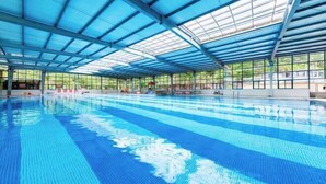 Una piscina interior con agua azul cristalina, una estructura cubierta y ventanas amplias.
