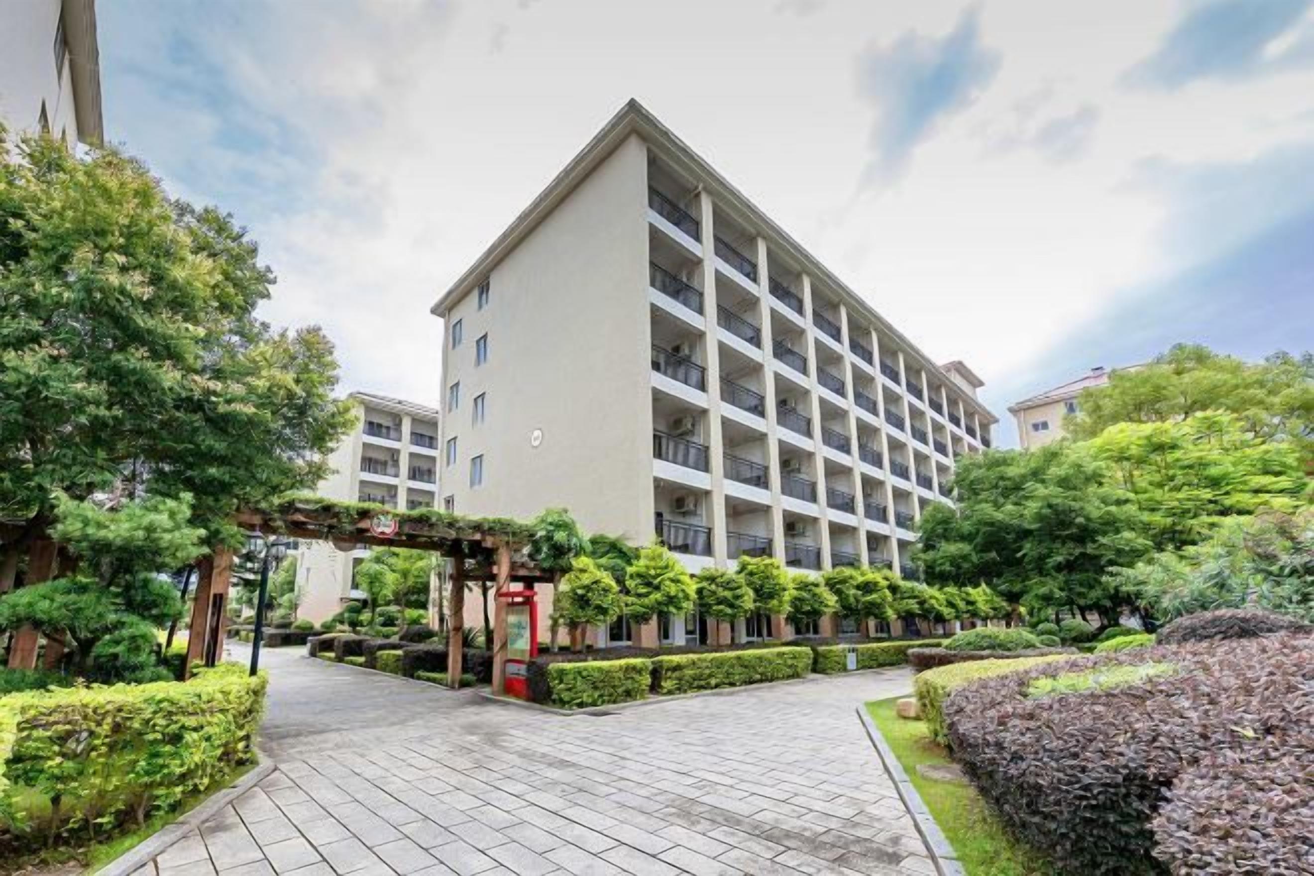 A multi-story hotel with a central courtyard, surrounded by well-maintained hedges and trees.