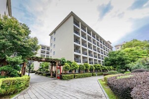 Un hotel de varios pisos con un patio central, rodeado de setos y árboles bien cuidados.