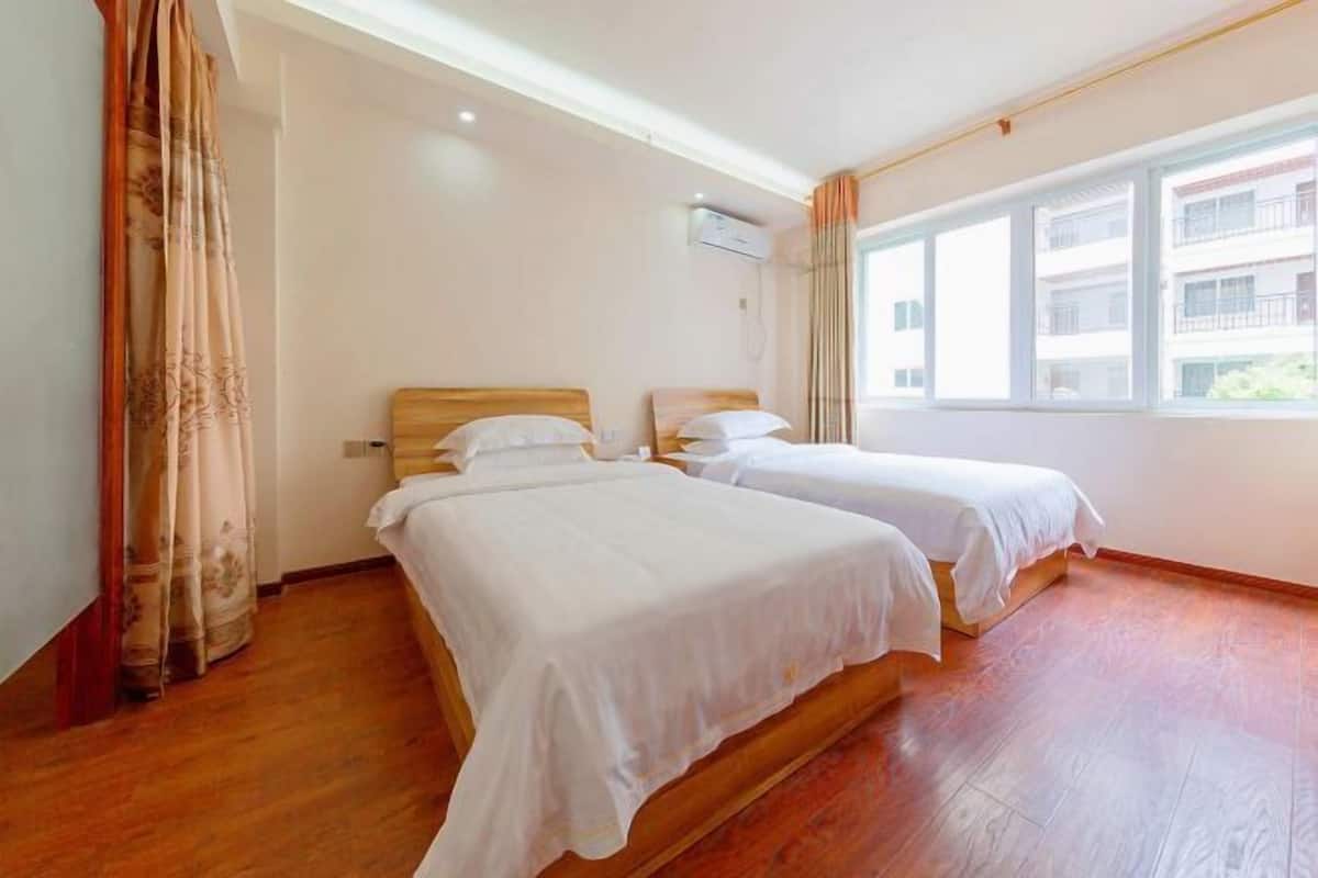Habitación de hotel con dos camas, piso de madera, ventana con vistas y aire acondicionado.