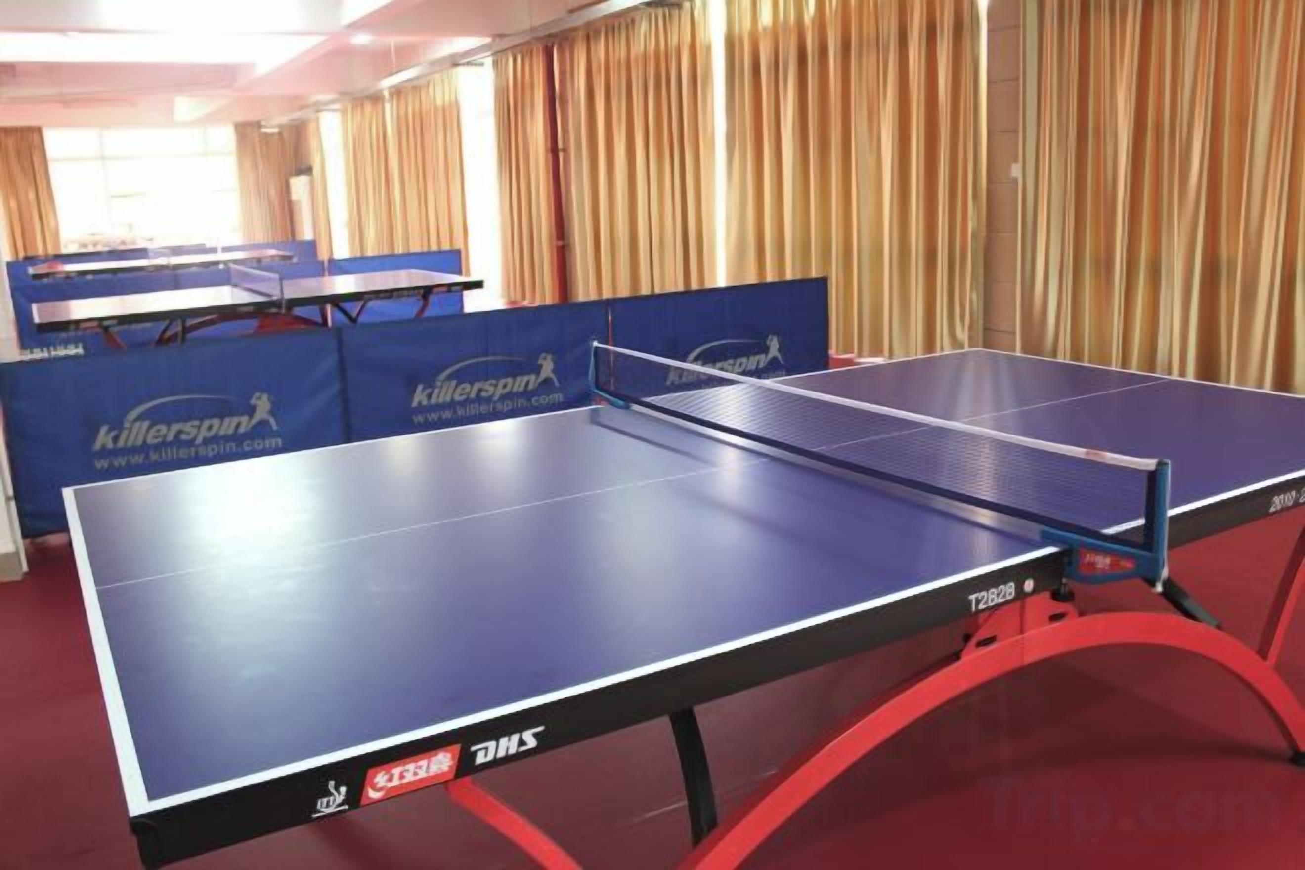 A ping pong table with a red frame and a net in a room with curtains.