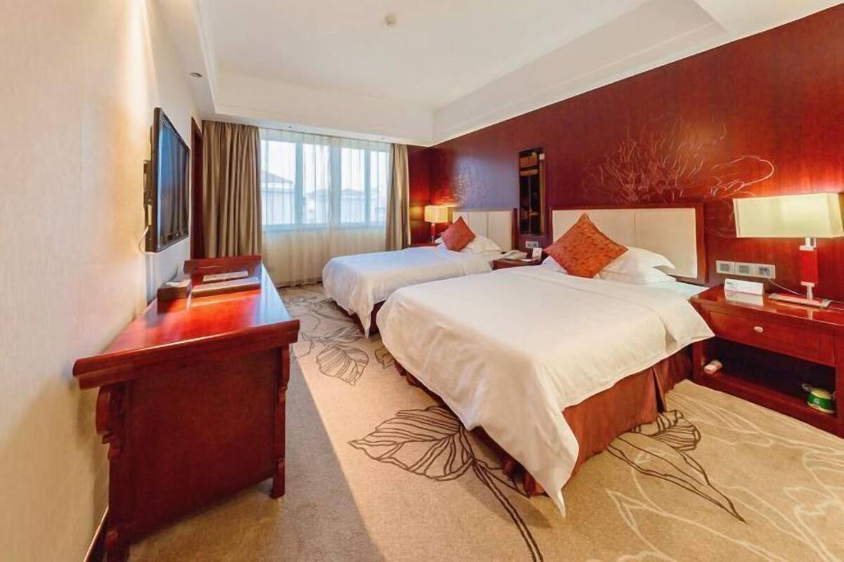 Habitación de hotel con dos camas, un escritorio, un televisor y una ventana con cortinas.