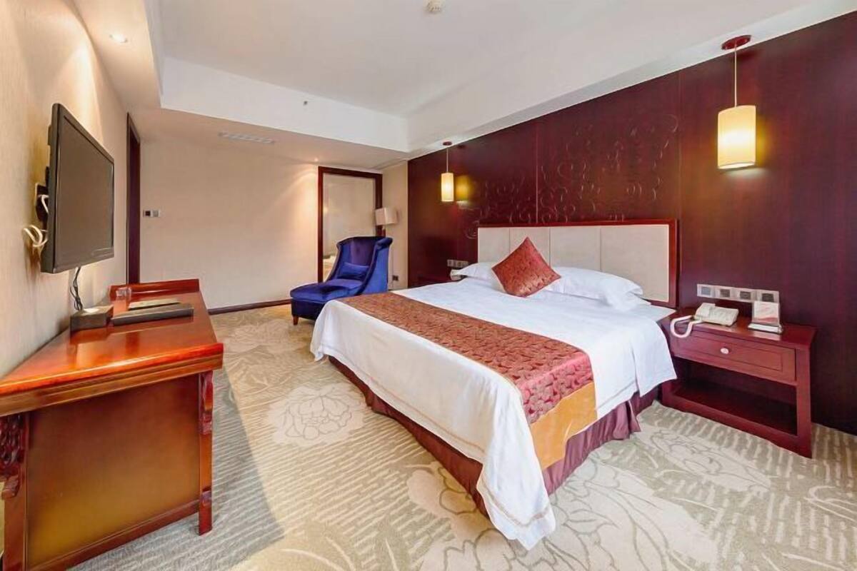 Habitación de hotel con una cama grande, un escritorio, una silla, un televisor y una mesita de noche con lámpara.