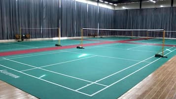 An indoor badminton court with a net, floor markings, and seating areas.