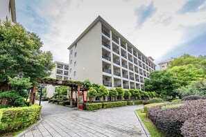 Hotel de vários andares com um pátio central, rodeado por vegetação e um céu claro.