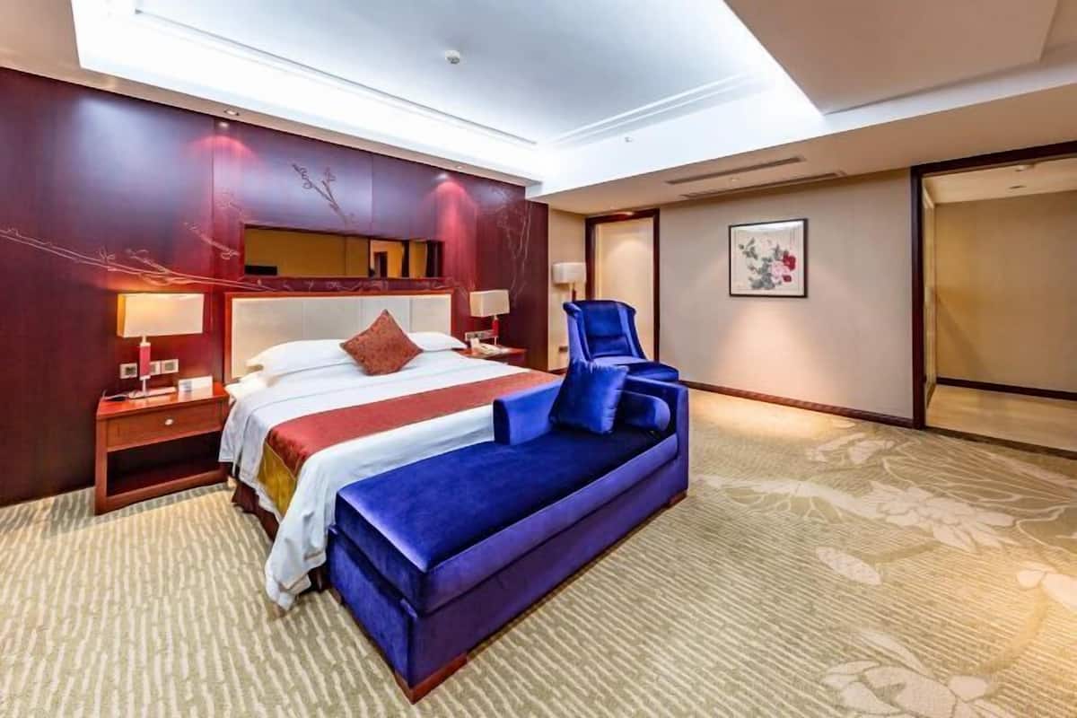 Una habitación de hotel con una cama grande, un sofá azul, una mesita de noche con lámpara y un televisor montado en la pared.