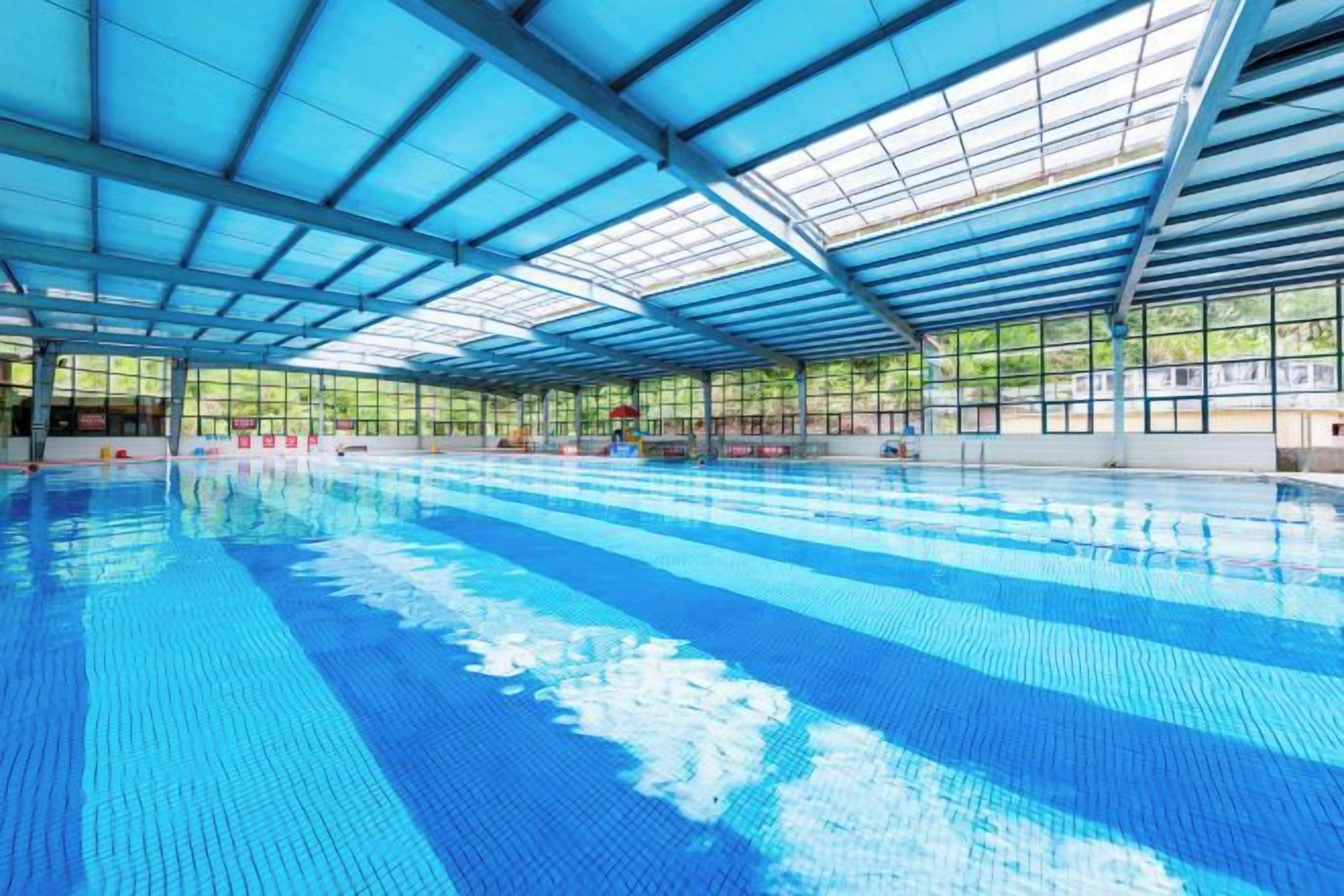 An indoor swimming pool with a clear roof structure and a tiled floor.