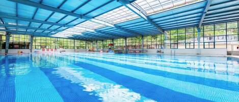An indoor swimming pool with a clear roof structure and a tiled floor.