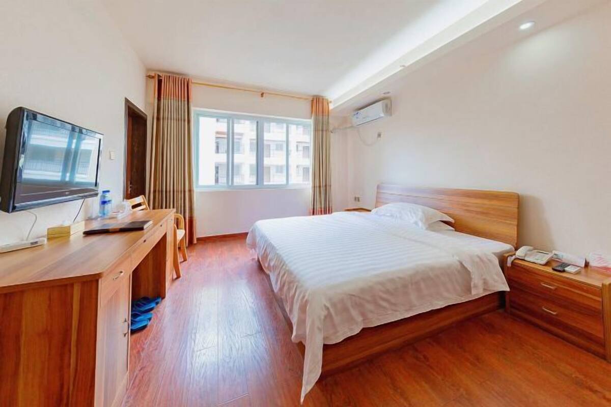 Habitación de hotel con cama, escritorio de madera, televisor y ventana con cortinas.