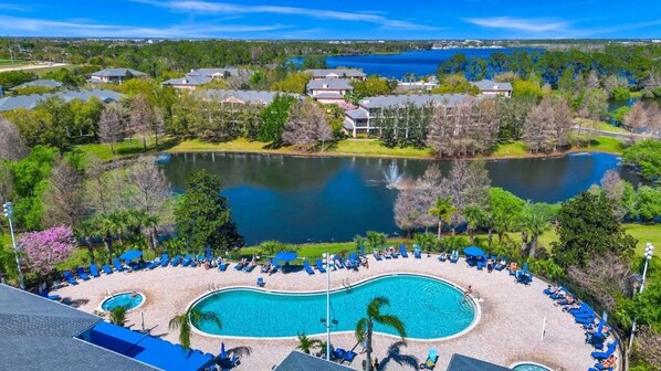 A resort with a large pool surrounded by lounge chairs and a lake.