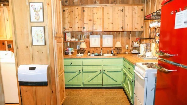Une cuisine avec des meubles de rangement en bois, un évier, une cuisinière et un réfrigérateur rouge.