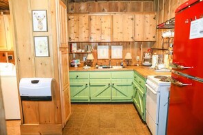 Eine Küche mit Holzschränken, einem Spülbecken, einem Herd und einem roten Kühlschrank.