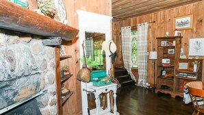 Une pièce chaleureuse avec une cheminée en pierre, des murs en bois, une console blanche et un escalier menant à un autre niveau.