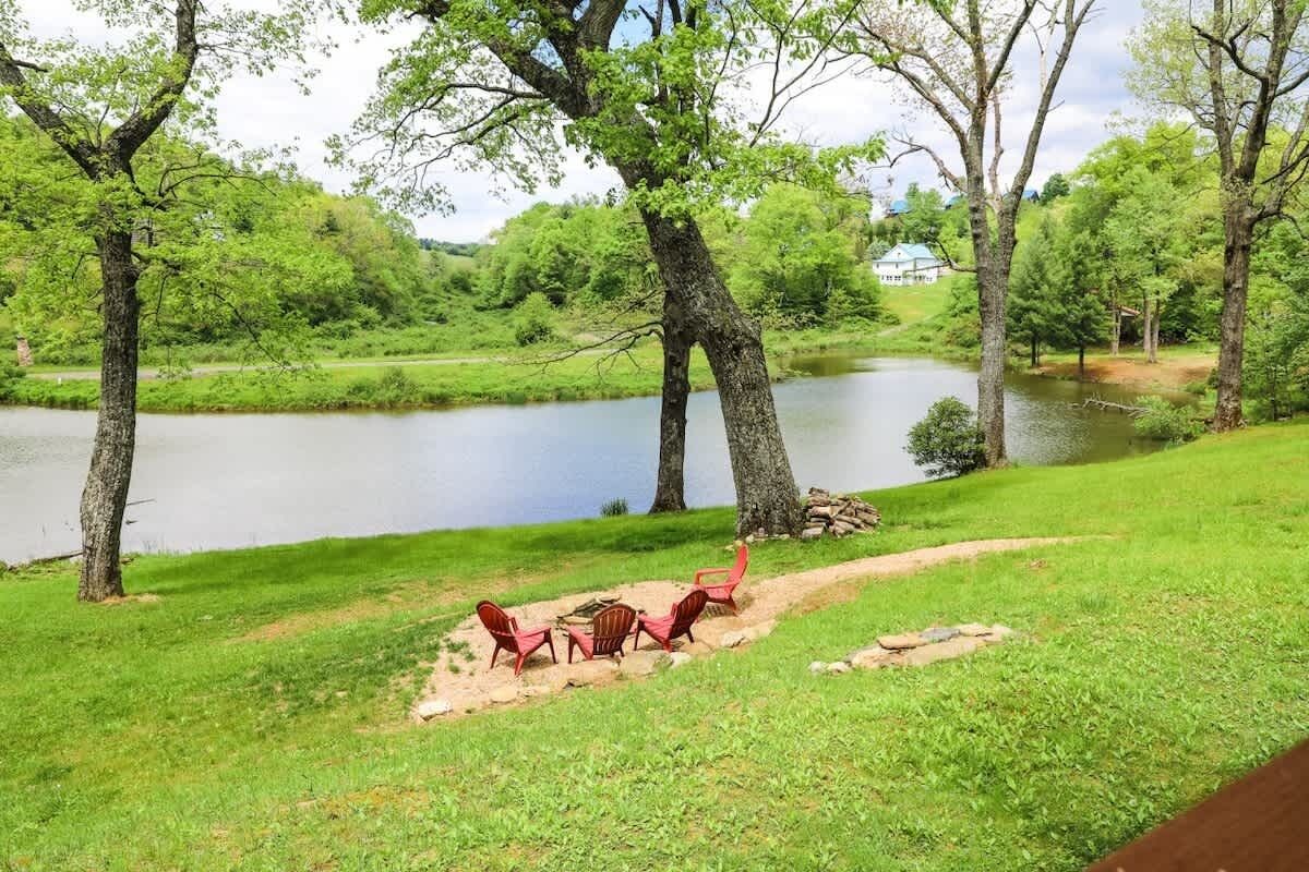 A lakeside view with a picnic area featuring red chairs and a fire pit.