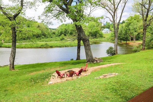 Vista del lago con zona de picnic que incluye sillas rojas y un brasero.