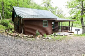 Une cabane en rondins dotée d’un porche, entourée d’une allée en gravier et d’un mur de pierres.