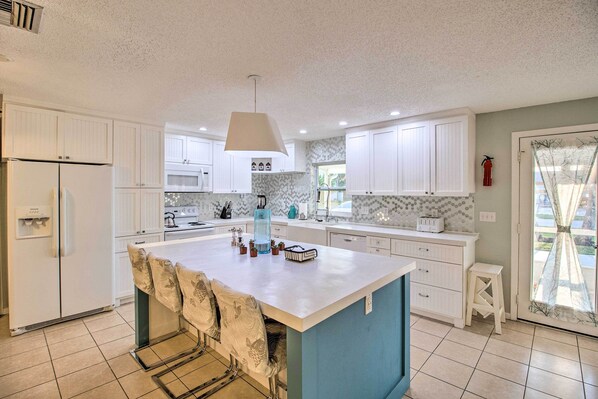 A modern kitchen with white cabinets, a central island, and a blue accent wall.