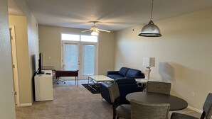 A living room with a sofa, a dining table with chairs, a small desk, and a ceiling fan. - Washburn Hotel Suites (Topeka)