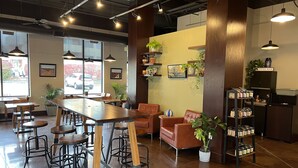 A modern cafe with a long wooden table, bar stools, a sofa, and a coffee bar. - Washburn Hotel Suites (Topeka)