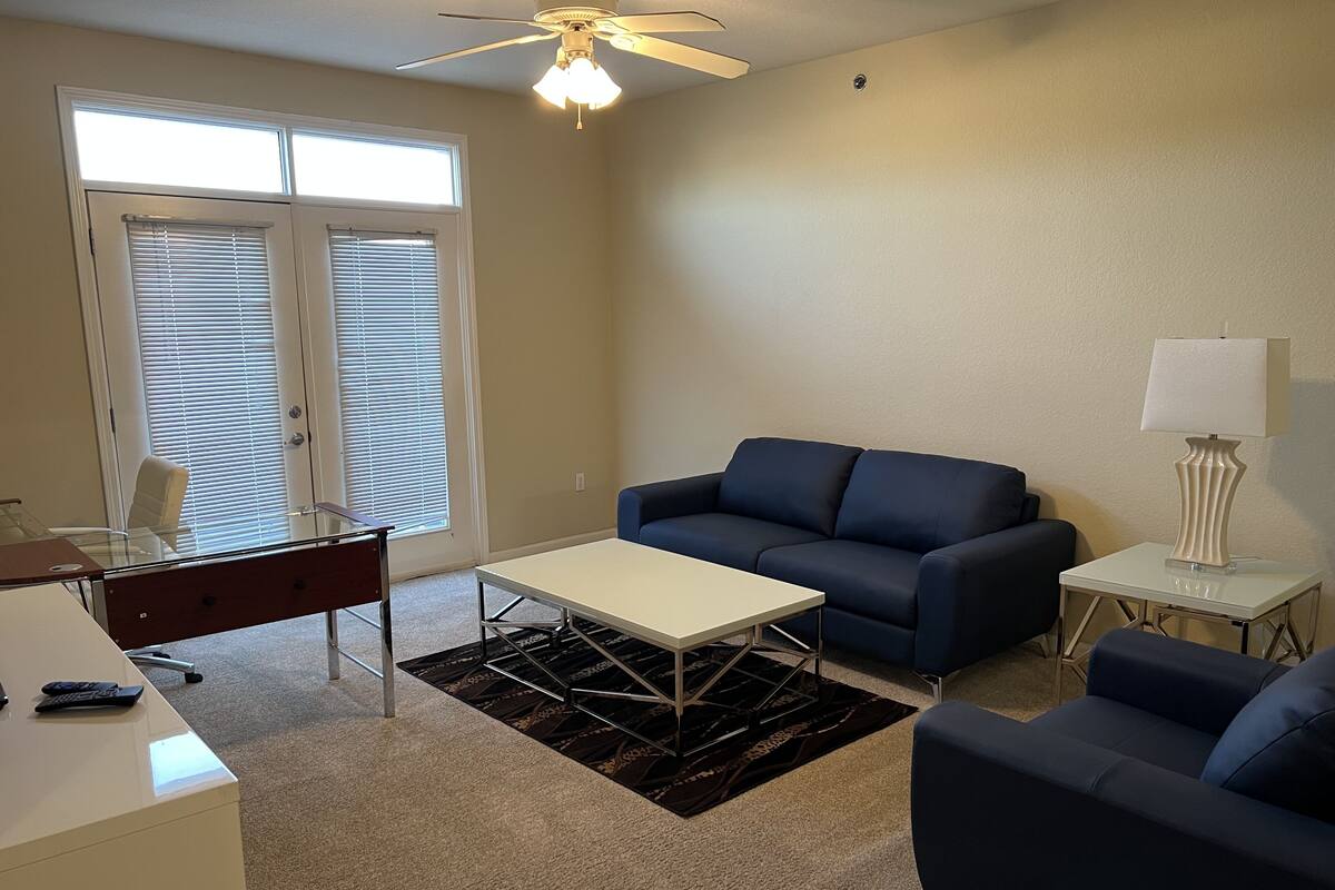 A living room with a blue sofa, a white coffee table, a desk with a chair, and a lamp on a side table.