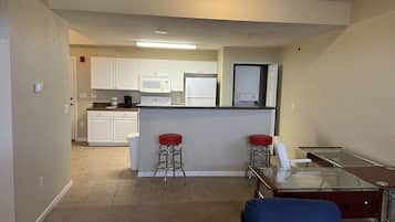 A compact living space with a kitchenette, a glass-top dining table, two red bar stools, and a blue sofa.