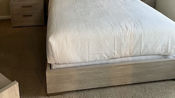 A neatly made bed with a wooden frame, two bedside tables with lamps, a ceiling fan, and a wall-mounted phone.