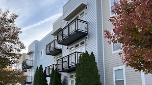 A multi-story residential building with balconies, a landscaped front yard, and a blue awning. - Washburn Hotel Suites (Topeka)