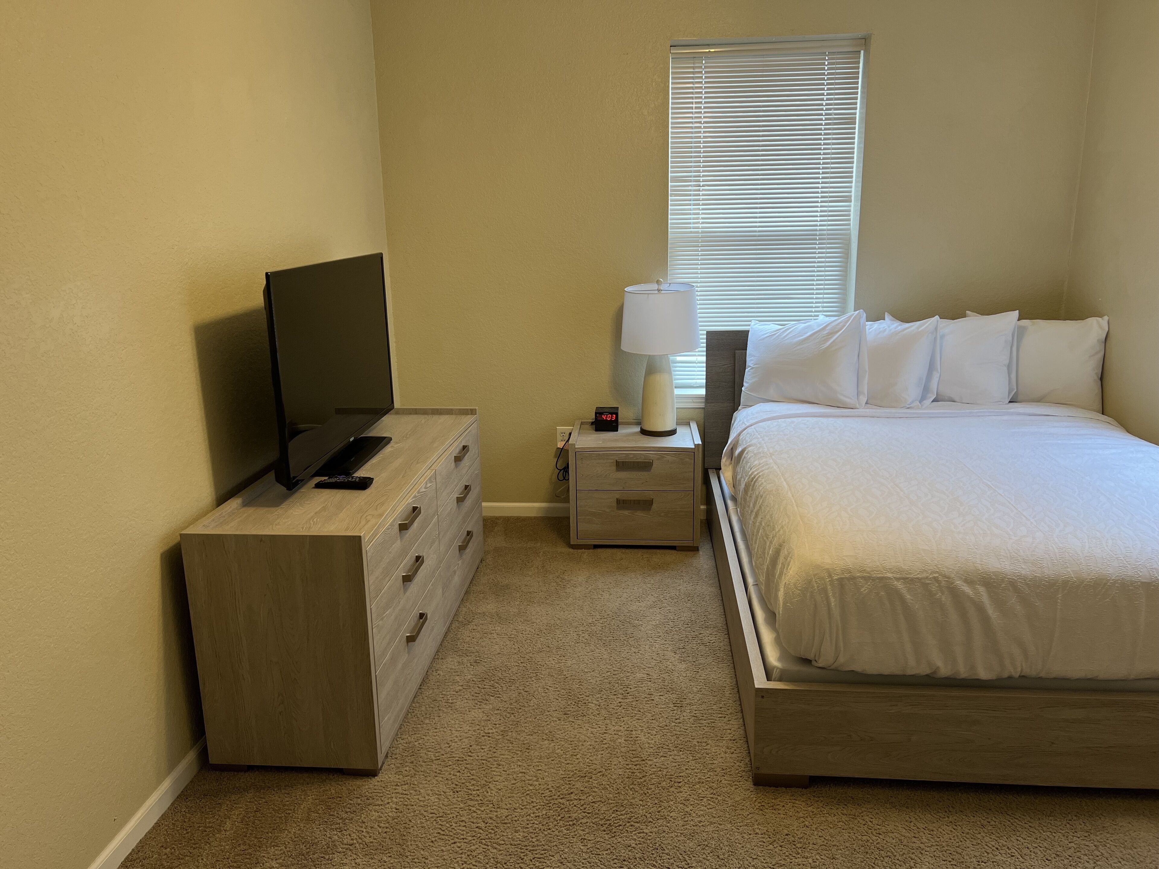 Een slaapkamer met een bed, een televisie, een dressoir, een nachtkastje en een lamp.