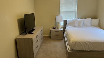 Een slaapkamer met een bed, een televisie, een dressoir, een nachtkastje en een lamp.