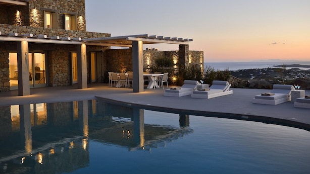 En modern villa med pool, utomhusmöbler och en fasad av sten.