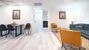 Ein modernes Wohnzimmer mit Essbereich, ausgestattet mit einer Couch, Sesseln, einem Couchtisch und Kunstwerken an den Wänden.