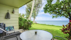 A patio with a round table and chairs, overlooking a lawn and the ocean.