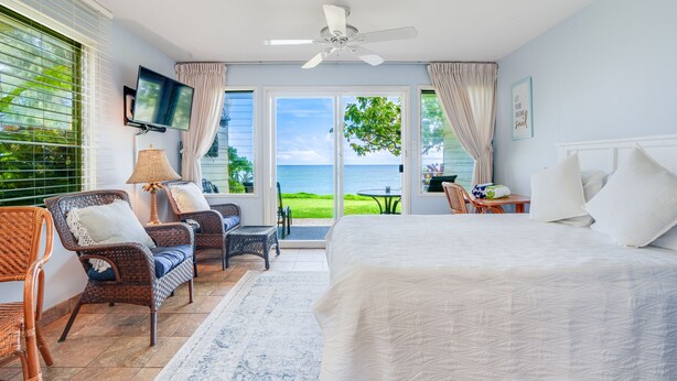A bedroom with a large bed, wicker chairs, a TV, and a view of the ocean.