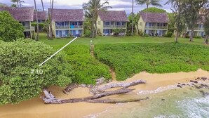 A beachfront property with multiple two-story buildings, a well-maintained lawn, and a sandy beach.