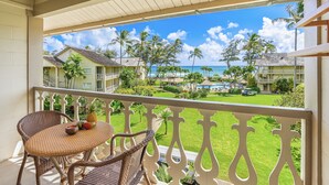 Un balcon agrémenté de fauteuils et d’une table en osier, donnant sur un complexe hôtelier avec des palmiers et une piscine.