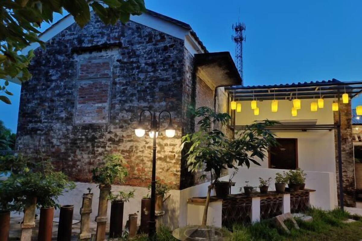 Un bâtiment rustique avec une façade en pierre, un balcon orné de guirlandes lumineuses et des plantes en pot au premier plan.
