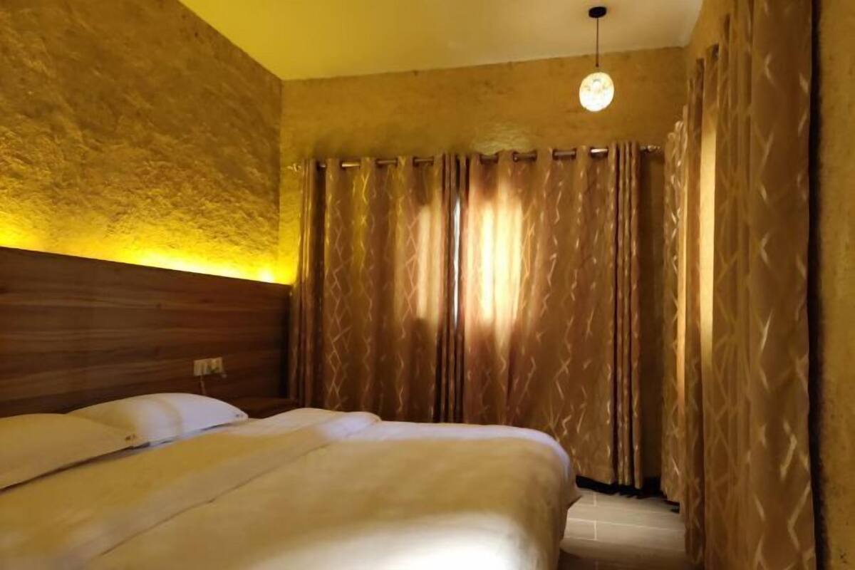 Une chambre d’hôtel avec une tête de lit en bois, un lit avec une literie blanche et un rideau orné d’un motif géométrique.