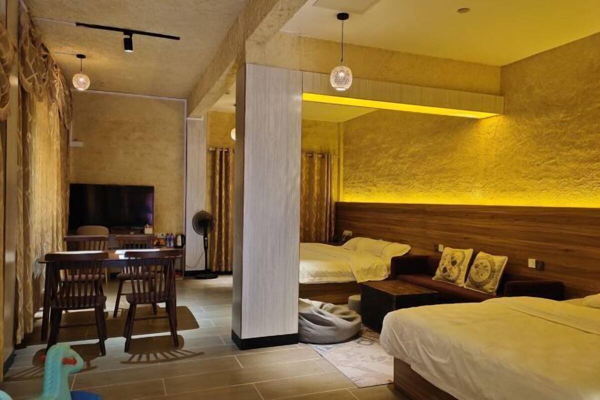 Une chambre d’hôtel avec une tête de lit en bois, un canapé, un coin repas avec des chaises et un téléviseur.