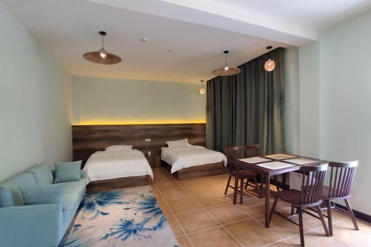 Une chambre d’hôtel avec deux lits simples, un canapé, une table à manger avec des chaises et une grande fenêtre avec des rideaux.