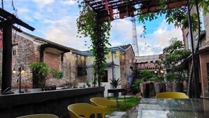 Un patio con una mesa larga y sillas, rodeado de muros de ladrillo y plantas en macetas.