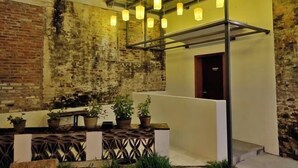 Un espacio al aire libre con una pared de ladrillo rústica, plantas en macetas y faroles colgantes.