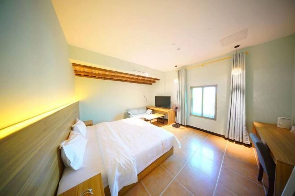 Une chambre d’hôtel équipée d’un lit, d’un bureau, d’une chaise, d’une télévision et d’une fenêtre avec des rideaux.