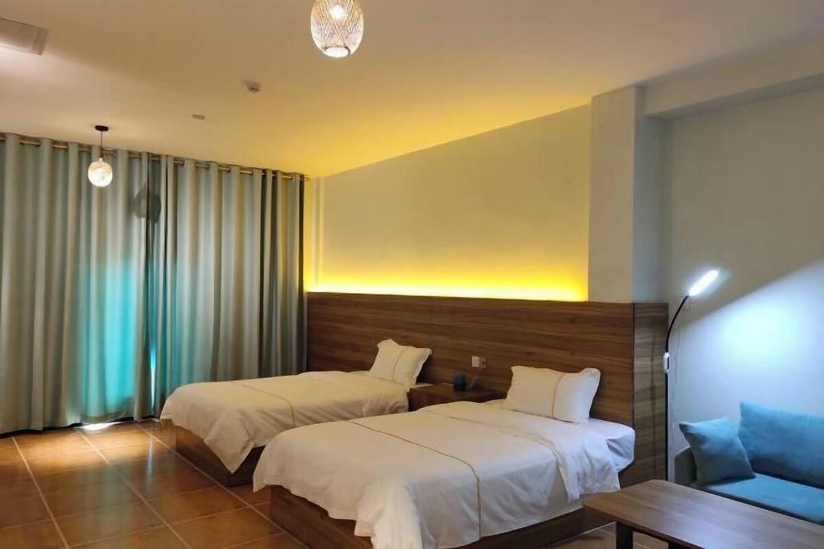 Une chambre d’hôtel avec deux lits, une tête de lit en bois, une table de chevet, une lampe et une vue sur l’extérieur.