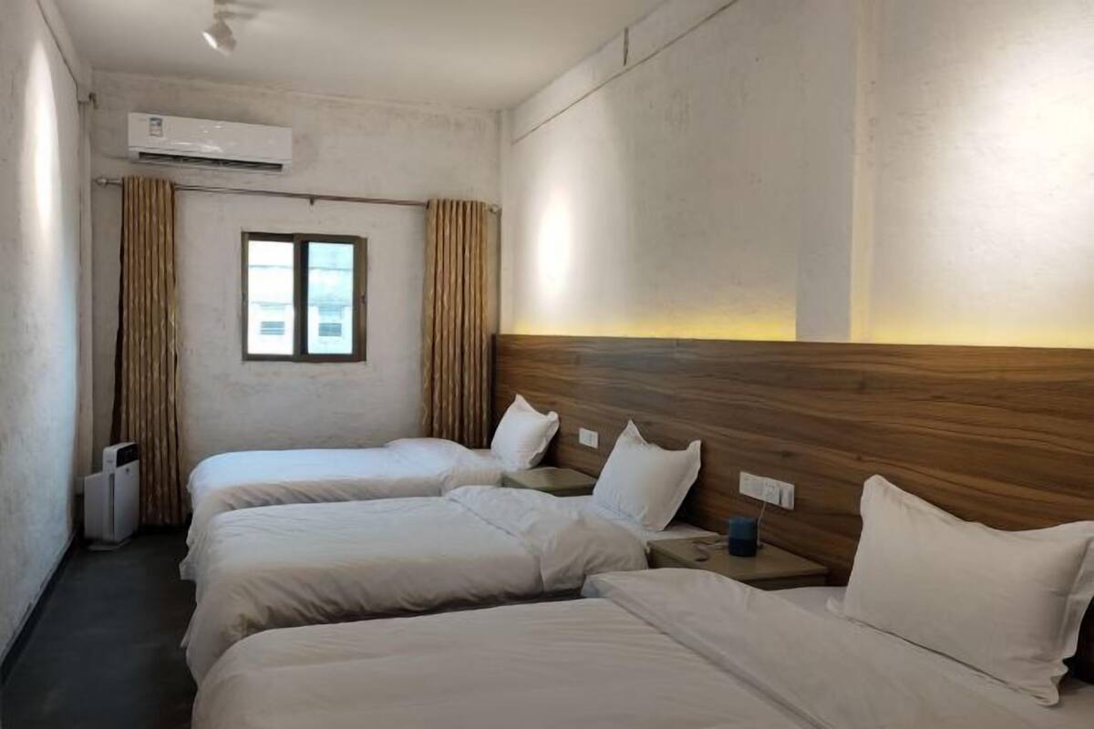 Une chambre d’hôtel avec deux lits simples, une tête de lit en bois, une fenêtre avec des rideaux et un appareil de climatisation.