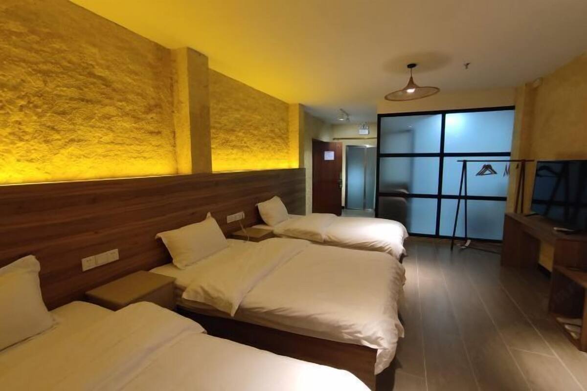 Une chambre d’hôtel avec trois lits, une tête de lit en bois et une grande fenêtre.