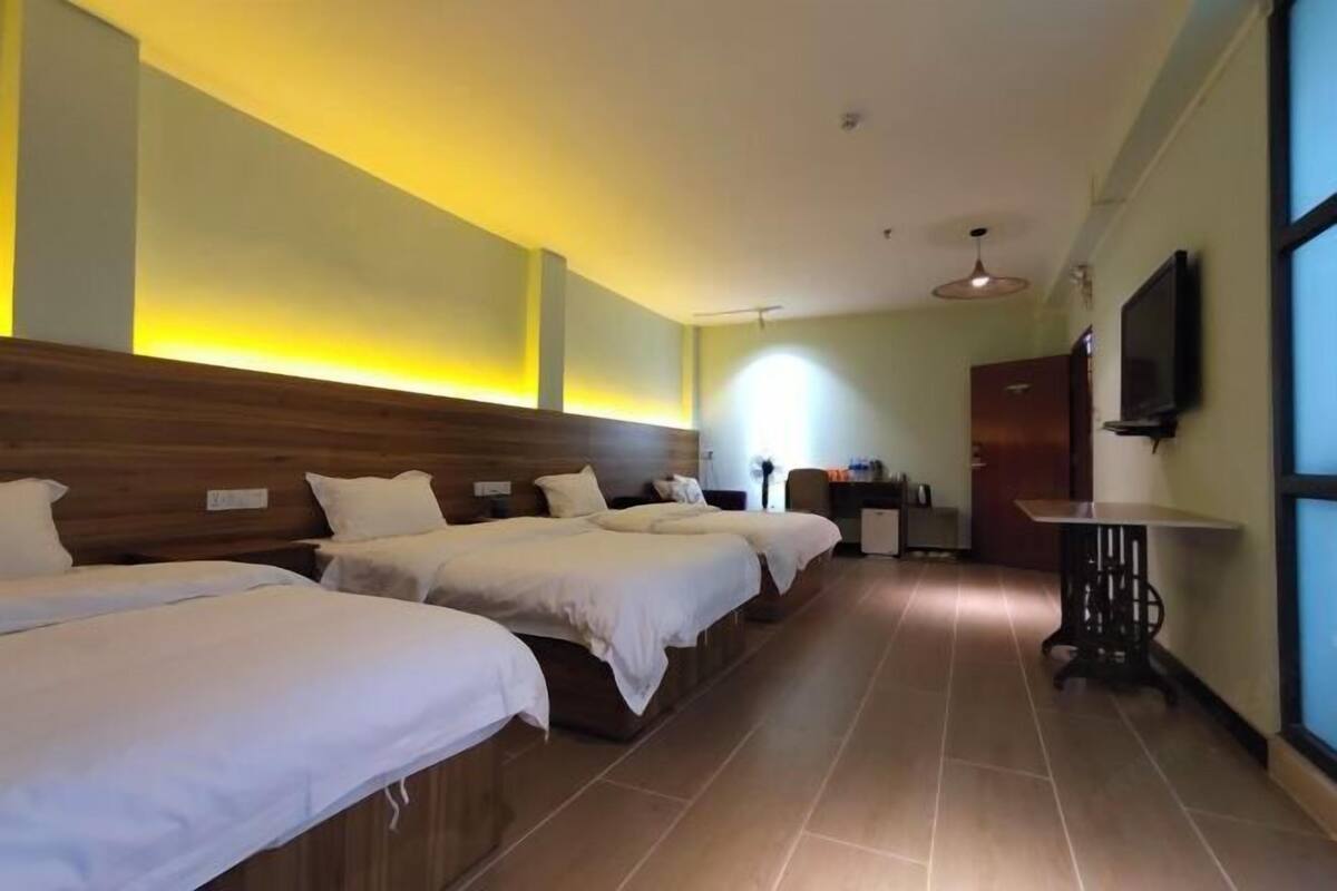 Une chambre d’hôtel avec trois lits, une télévision, un bureau et une fenêtre.