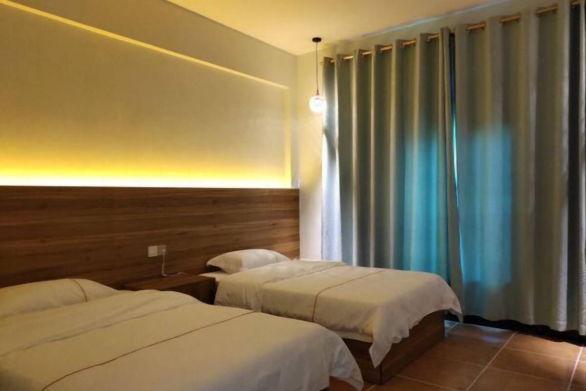 Une chambre d’hôtel avec deux lits, une tête de lit en bois, une lampe fixée au mur et une fenêtre avec des rideaux.