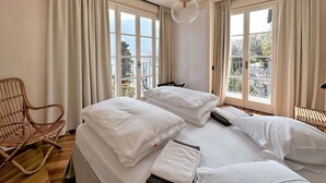 Una camera da letto con due letti, una sedia in vimini e vista sull'esterno attraverso ampie finestre.